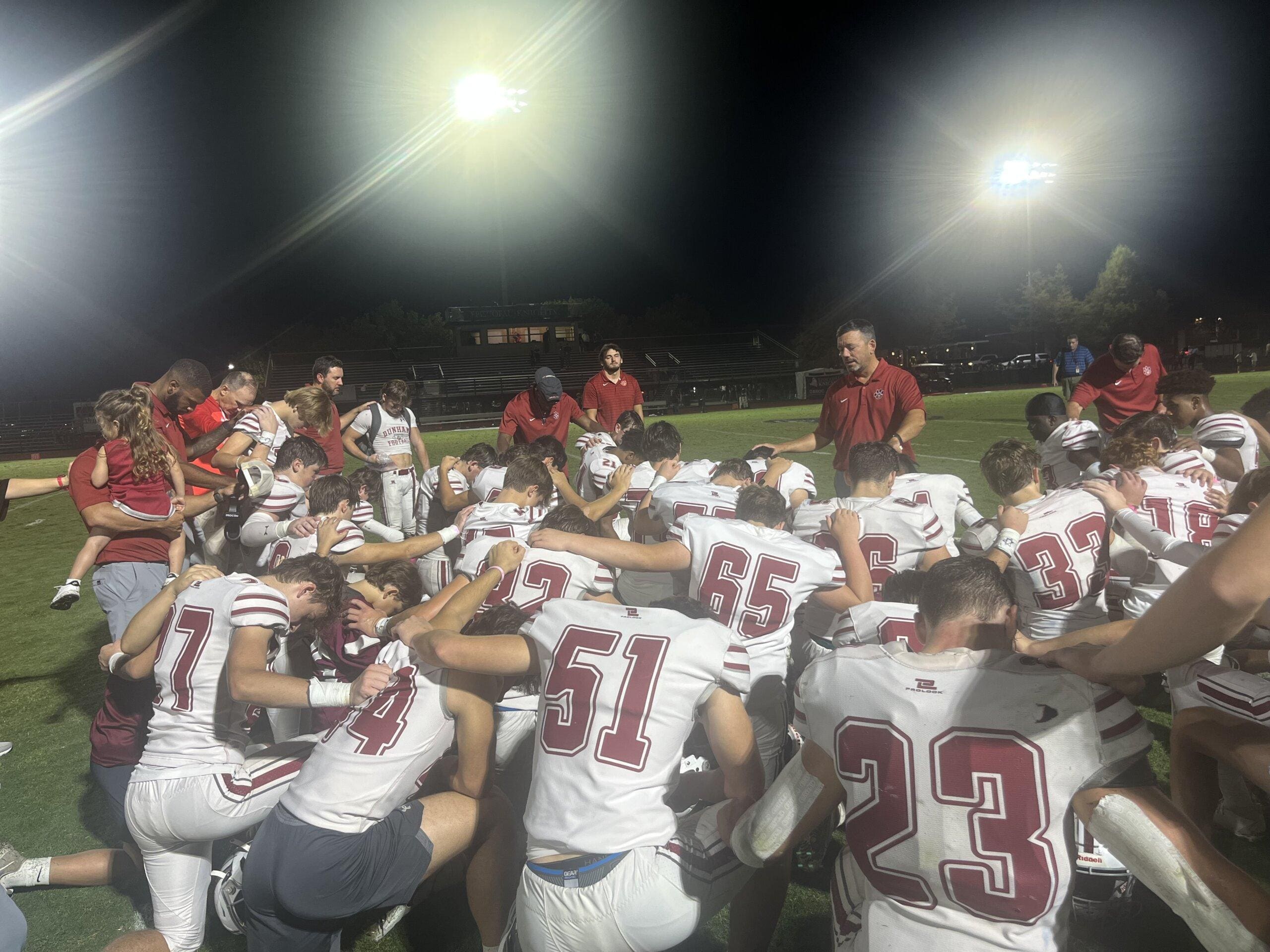 Football team huddles with coach at night.